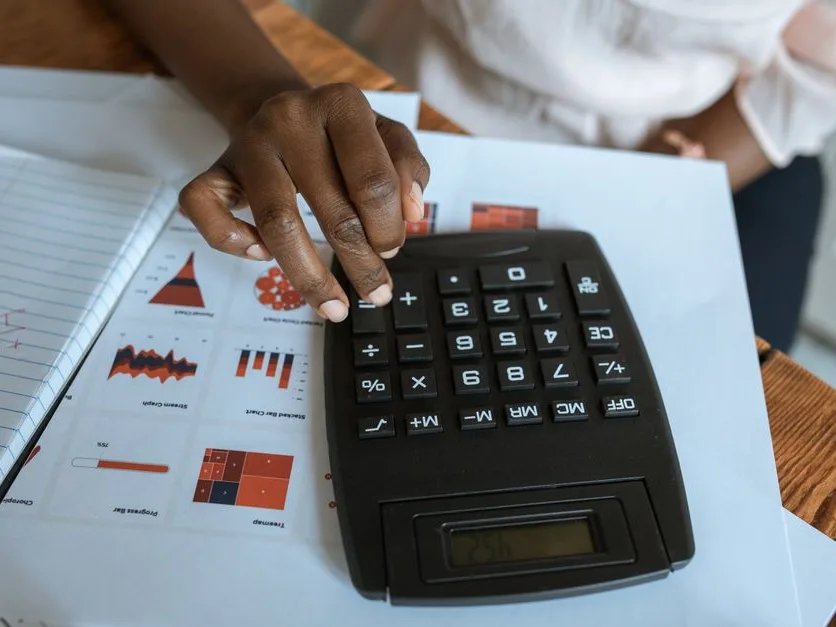 Mains sur une calculatrice devant des tableaux de chiffres